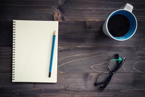 Office wood table with blank notepad, pencil, glasses and cup of coffee. photo