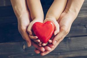 Close up mother and children hands giving red heart on wood background photo