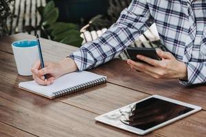 woman hand writing notepad and holding phone on wooden table at coffee shop photo