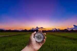 A man holding compass on hand at field and sunset for navigation guide. photo