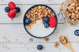 bowl of granola with yogurt, fresh berries, strawberry on wood table. photo