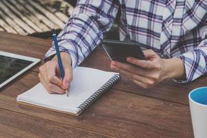 asia woman writing and holding phone on wood table in coffee shop photo