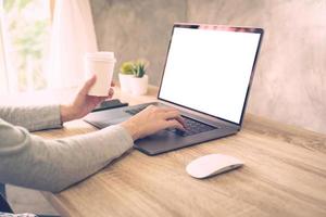 Woman holding coffee and using laptop on wooden table in office photo