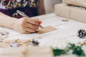 cerca arriba de manos mujer escritura vacío lista de deseos y Navidad tarjeta en de madera mesa con Navidad decoración. foto