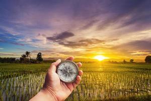 A man holding compass on hand at field and sunset for navigation guide. photo