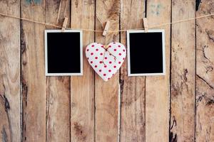 White heart and two photo frame hanging on clothesline rope with wooden background.