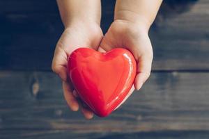 Close up children hands giving red heart on wood background photo