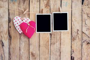 Two heart and two photo frame hanging on clothesline rope with wooden background.