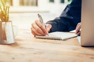 Asia man hand writing notebook paper on wood table in coffee shop with vintage toned filter. photo