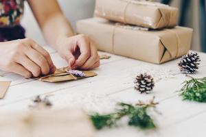 Close up of hands holding wrapping gift box and christmas card on wooden table with xmas decoration. photo