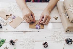 Close up of hands holding wrapping gift box and christmas card on wooden table with xmas decoration. photo