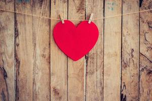 Red heart hanging on clothesline and rope with wooden background photo