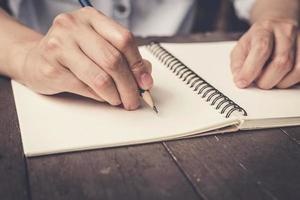 cerca arriba mano mujer escritura cuaderno en madera mesa antecedentes. foto