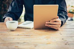 Business man hand holding tablet on table in coffee shop with vintage toned filter. photo