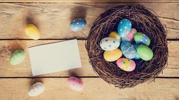 vistoso Pascua de Resurrección huevo en nido y papel tarjeta en madera antecedentes con espacio. foto