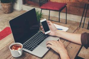 Business man holding phone and using laptop on wooden table. Vintage toned. photo