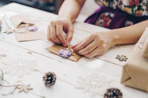 Close up of hands holding wrapping gift box and christmas card on wooden table with xmas decoration. photo