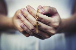 mujer manos Orando participación un rosario rosario con Jesús Cristo en el cruzar o crucifijo en negro antecedentes. foto