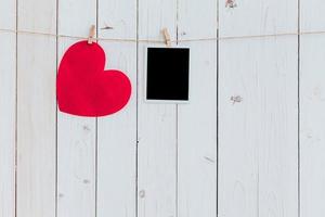 Red heart and photo frame blank hanging at clothesline on wood white background with space. Valentine Day.