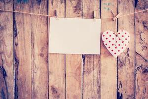 Heart fabric and paper hanging on clothesline at wood background with space. photo