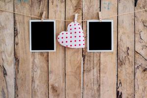 White heart and two photo frame hanging on clothesline rope with wooden background.