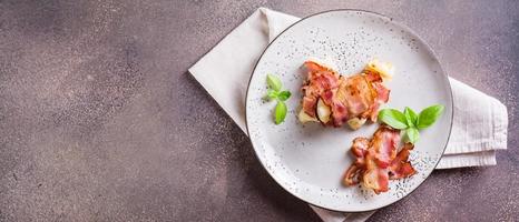 Rolls of fried bacon and mashed potatoes and basil on a plate on the table. Top  view. Web banner photo