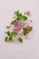 A bottle of women's perfume or toilet water lies among the flowers of an apple tree on a pink background. perfume template. product presentation. photo