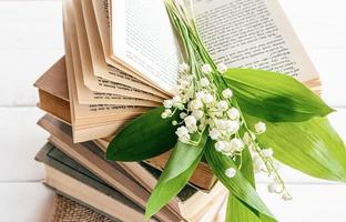 a stack of old books and a bouquet of spring lilies of the valley on an open book. front view. spring composition with flowers. good morning mood. photo