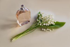 an elegant bottle of cosmetic or perfume stands on a beige background with a bouquet of May lilies of the valley. the concept of beauty, freshness. photo