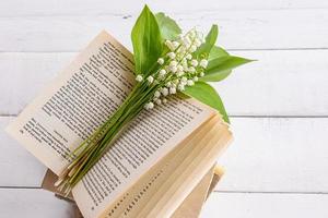 un ramo de flores de delicado fragante lirios de el Valle mentiras en un abierto libro y un blanco de madera mesa. el concepto de un bueno ánimo, un primavera Mañana. foto