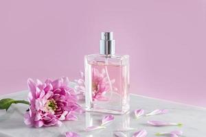 un elegante botella de De las mujeres perfume o rociar soportes en parte de un blanco mármol podio y un rosado antecedentes. frente vista. el concepto belleza. foto