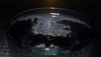 macro coup une chute laissez tomber de l'eau dans une verre contre une noir Contexte. lent mouvement. video