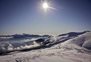 Bright sun above snowy mountain slopes and clouds landscape photo