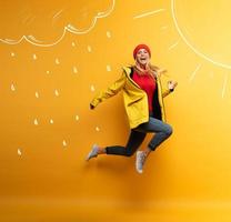 Girl with jacket jumps to the sun from the rainy weather. Joyful expression. Yellow background photo