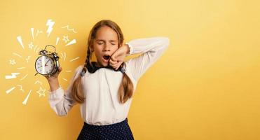 Young child student with ringing alarm clock is lazy going to school. Yellow background photo