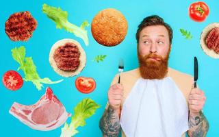 Man with tattoos is ready to eat with cutlery in hand. cyan background photo