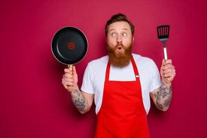 sorprendido cocinero con barba y rojo delantal es Listo a cocinar foto