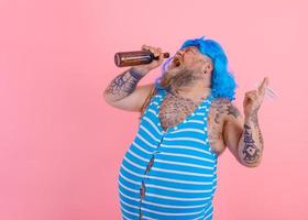 Fat man with beard and wig smokes cigarettes and drinks beer photo