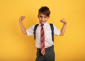 Young boy student acts like a muscled man. Yellow background photo