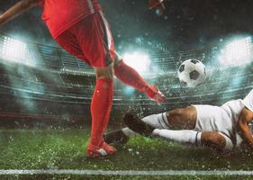 Soccer scene at the stadium with player in a red uniform kicking the ball and opponent in tackle to defend photo