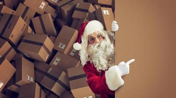 Santa Claus indicates a space for the Christimas present, with ready packages on background photo