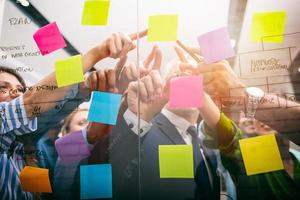 Team of people at work in the office indicates with their hand an adhesive note on the glass photo