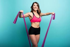 Determinated girl trains with elastic for gym. Happy and joyful expression. Cyan background photo
