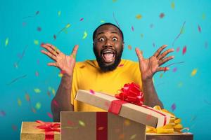 Happy and amazed man opens gifts on his birthday. Isolated on cyan background photo