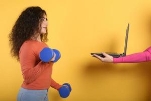 Girl with handlebars ready to start the gym online with a computer. yellow background photo