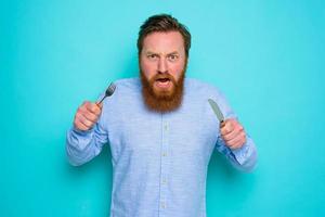 Hungry man with tattoos is ready to eat with cutlery in hand photo