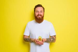 Happy man with beard and tattoos holds an avocado photo