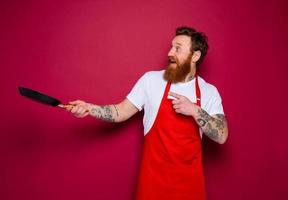 amazed chef with beard and red apron cooks with pan photo