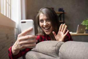 mujer empieza un vídeo llamada con su teléfono inteligente en el sofá foto