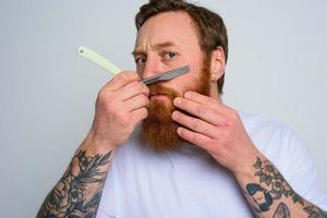 Serious man with blade is focused on cutting his beard photo